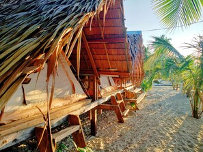 Una cabaña en la playa con techo de paja, bancos de madera y un camino de arena.