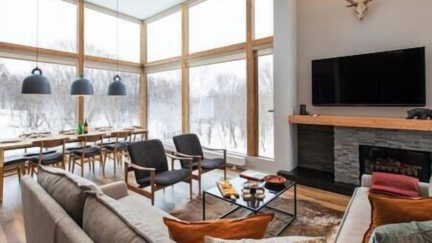 Ein geräumiges Wohnzimmer mit großem Fenster, Kamin und einem Wand-Fernseher.
