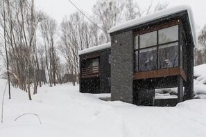 A modern house with a stone facade and large windows, surrounded by snow-covered trees. - Ukiyo | 3BR - Niseko Village Chalet near Annupuri Slopes (Niseko)