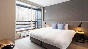 Ein modernes Schlafzimmer mit einem großen Bett, einem Nachttisch und einem Fenster mit Blick auf Bäume.