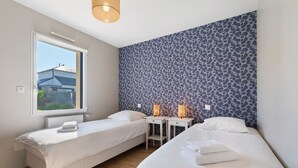 Une chambre avec deux lits simples, une fenêtre, un radiateur et un mur décoré de motifs.