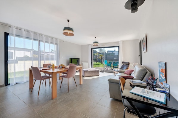 Un salon moderne comprenant un coin repas, un canapé, un bureau avec un ordinateur et de grandes fenêtres.
