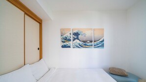 Habitación de hotel con una cama, una obra de arte en la pared de una ola, y una puerta de madera.