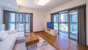 Una sala de estar moderna con sofá, mesa de centro, televisor y ventanas amplias con vistas a la ciudad.