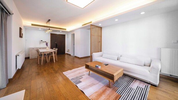 Una sala de estar moderna con un sofá blanco, una mesa de centro de madera y un comedor con una mesa y sillas blancas.