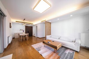 A modern living room with a white sofa, wooden coffee table, and a dining area with a white table and chairs. - Tyms 3BR 2BA Apt Near Metro (Shanghai)