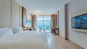 A hotel room with a large bed, a desk, a chair, a TV, and a balcony with a view. - Homie Panorama Beachfront Residences Nha Trang (Nha Trang)