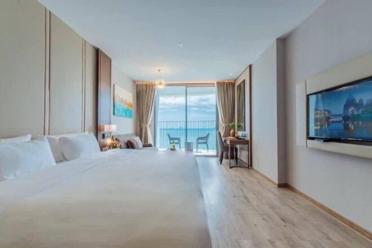 Ein Hotelzimmer mit einem großen Bett, einem Schreibtisch, einem Sessel, einem Fernseher und einem Balkon mit Blick.