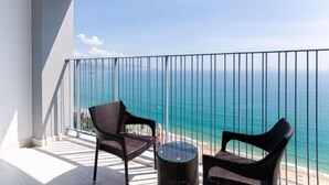 A balcony with two wicker chairs and a small round table, overlooking a beach with clear blue water. - Homie Panorama Beachfront Residences Nha Trang (Nha Trang)