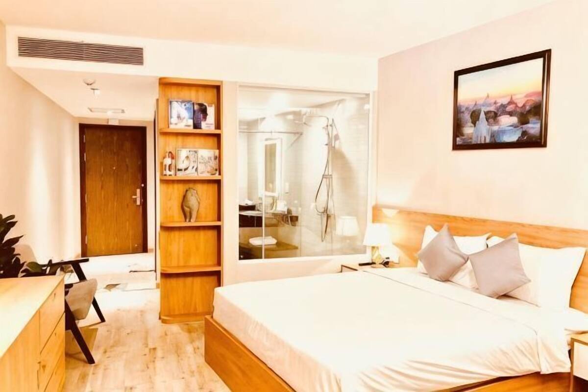 Ein Schlafzimmer mit Bett, einer Holzregal-Einheit, einem Badezimmer mit Glasdusche und einem Gemälde an der Wand.