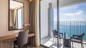 A hotel room with a desk, chair, and a balcony with a view of the sea. - Homie Panorama Beachfront Residences Nha Trang (Nha Trang)
