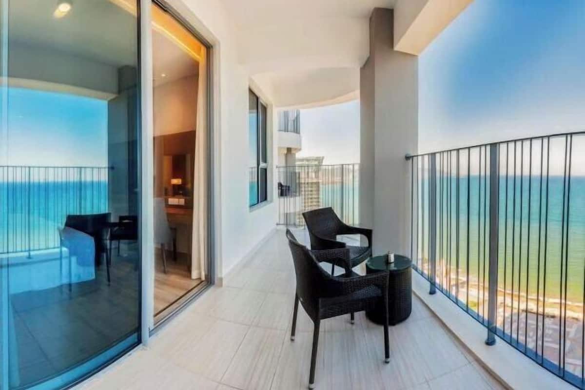 Ein Balkon mit Meerblick, eine Glastür, die zu einem Zimmer führt, und ein Tisch mit Stühlen.