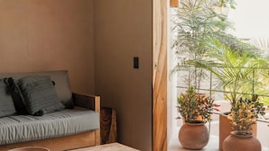 A cozy room with a wooden table, a woven chair, a cushioned bench, and potted plants by a window. - Punta Morelos (Brisas de Zicatela)