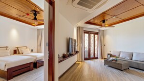 A hotel room with two beds, a sofa, a TV, and a ceiling fan. - Hoi An Eco Retreat (Da Nang)