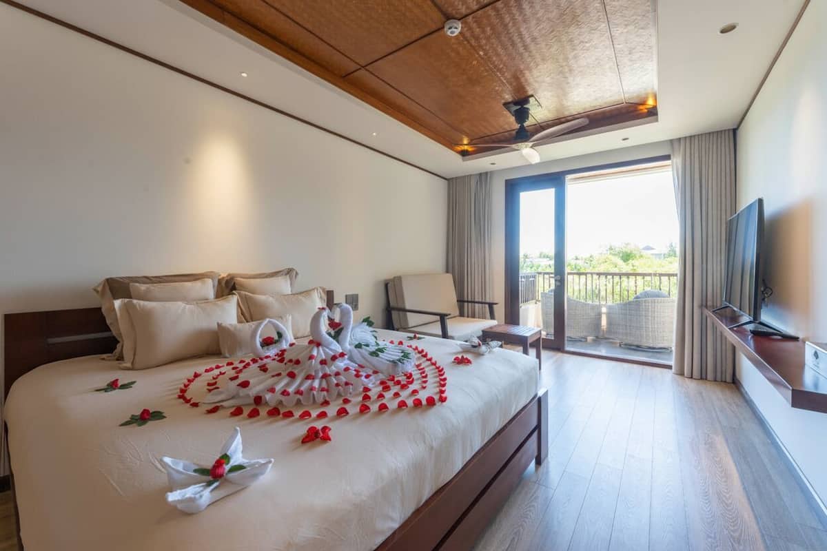 Una camera d'albergo con un letto grande, un balcone con vista, una TV e un ventilatore a soffitto.