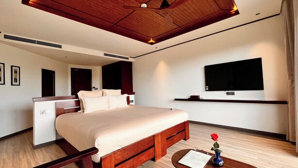 Ein modernes Hotelzimmer mit einem großen Bett, einem Schreibtisch, einem Flachbildfernseher und einer Holzbalkendecke.
