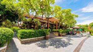 A covered outdoor area with a stone pathway leading to a building, surrounded by lush greenery and a clear sky. - Hoi An Eco Retreat (Da Nang)
