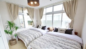 A hotel room with two beds, large windows with curtains, a potted plant, and a hanging light fixture. - ITOMAN IN (Itoman)