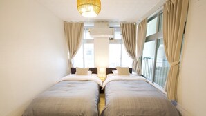 A twin room with two beds, a hanging light fixture, and large windows with curtains. - ITOMAN IN (Itoman)