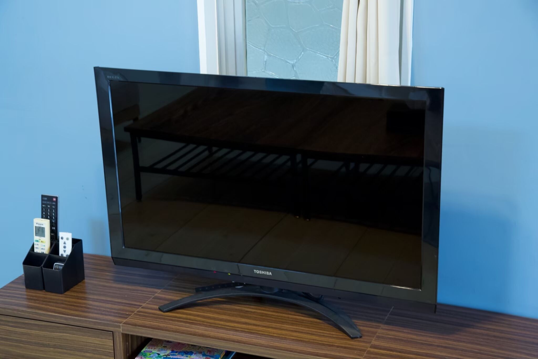 Een flatscreen televisie op een houten standaard, met een houder voor de afstandsbediening ernaast.