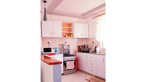 A kitchen with white cabinets, a stove, a microwave, and a red towel hanging on the oven door. - Eve's Vista 2 bedroom apartment, Nanyuki- Kenya (Nanyuki)