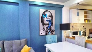 A modern living room with a blue accent wall, a large abstract painting, a grey sofa, and a white dining table. - Eve's Vista 2 bedroom apartment, Nanyuki- Kenya (Nanyuki)