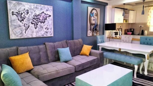 A modern living room with a grey sofa, colorful cushions, a white coffee table, and a dining table with blue chairs. - Eve's Vista 2 bedroom apartment, Nanyuki- Kenya (Nanyuki)