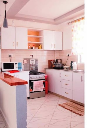 Une cuisine avec des meubles blancs, une cuisinière, un four à micro-ondes et un torchon rouge accroché à la porte du four.