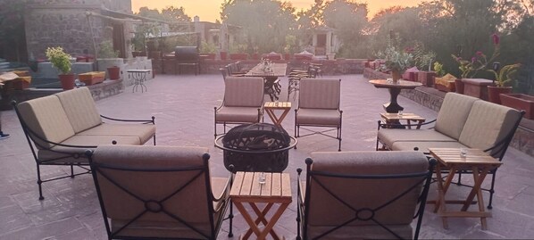 An outdoor seating area with tables and chairs, a fire pit, and potted plants. - Rawla Anand Rohet (Rohat)