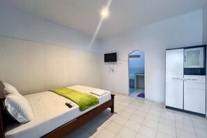 A single bed with a green blanket, a white pillow, a mounted TV, and a wardrobe in a room with white walls and tiled flooring. - SN Guest House near Trans Studio Mall Bali (Bali)