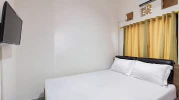 A hotel room with a bed, a flat-screen TV, and a window with curtains.