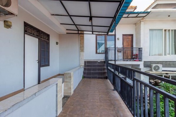 A covered corridor with a staircase leading to a balcony, a door, and an air conditioning unit.