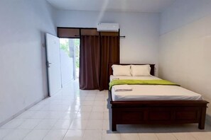 A bedroom with a bed, a window with curtains, an air conditioning unit, and a door. - SN Guest House near Trans Studio Mall Bali (Bali)