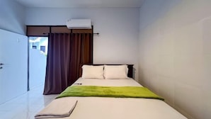 A single bed with a green blanket, a white pillow, and a brown curtain.