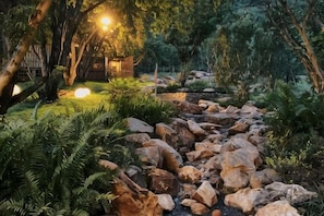 Een tuin met een pad van stenen, bomen en een klein gebouw met verlichting.