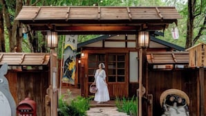 A traditional wooden structure with a covered entrance, stone pathway, and a decorative owl statue. - Tanuki house Khaoyai (Pak Chong)