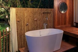 Een wellnessruimte met een groot vrijstaand bad, houten lambrisering en een spiegel.