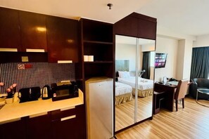 Et kompakt hotelværelse med tekøkken, seng, skrivebord og tv.