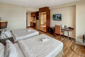 Hotellihuone, jossa on kaksi sänkyä, työpöytä, tuoli, televisio ja pieni keittokomero.