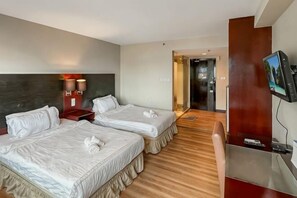 Hotellihuone, jossa on kaksi sänkyä, työpöytä, televisio ja puulattia.
