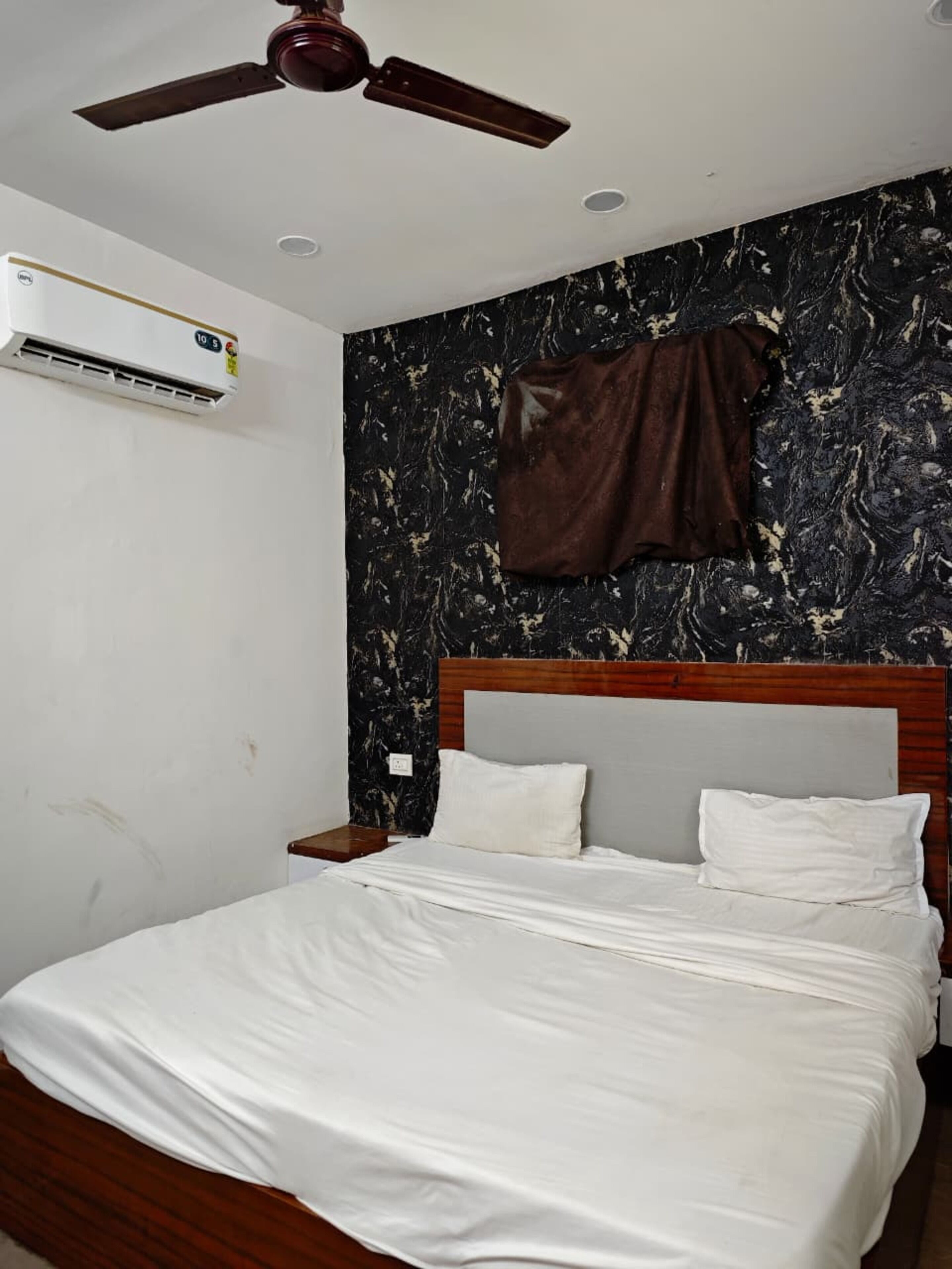 A bedroom with a bed, a ceiling fan, an air conditioning unit, and a marble-patterned wall.