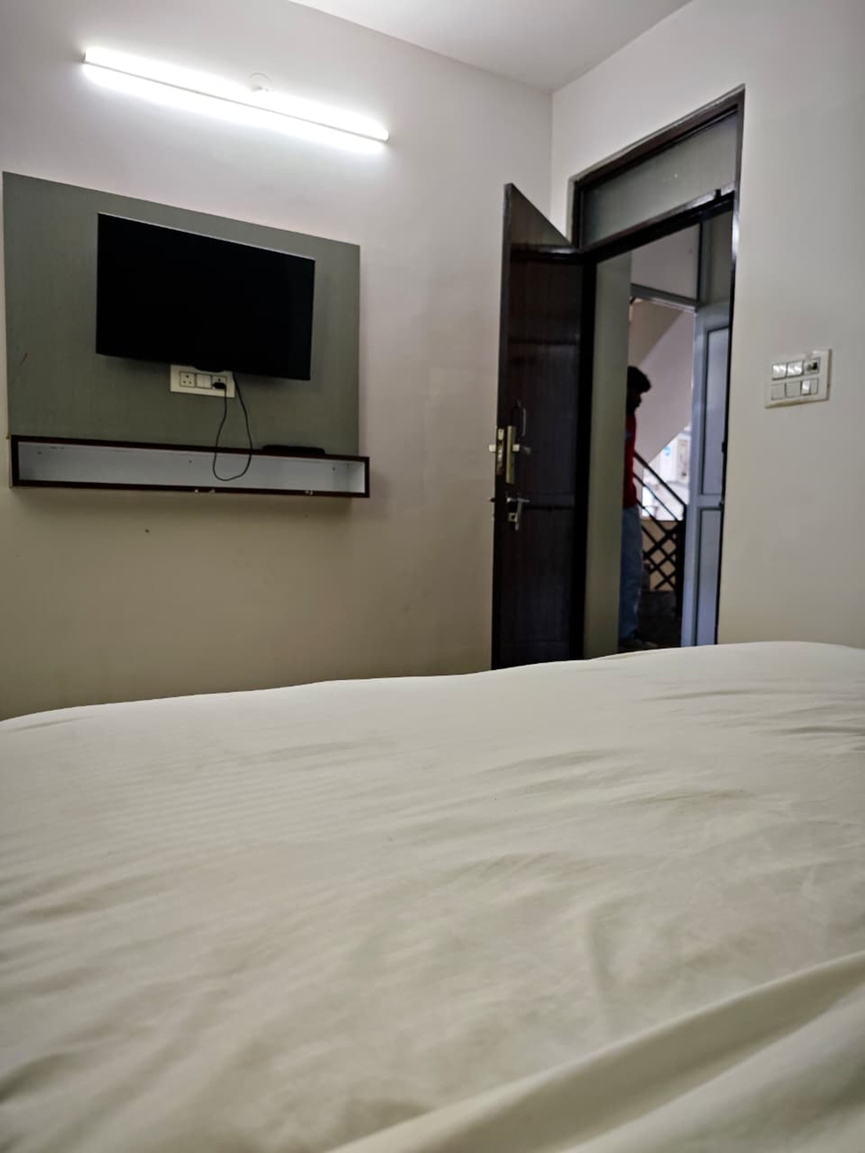 A hotel room with a bed, a flat-screen TV mounted on the wall, and a door leading to another room.
