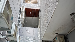 Un carrer estret amb una petita zona de recepció, diversos equips de aire condicionat i una porta de fusta que dona a una habitació.
