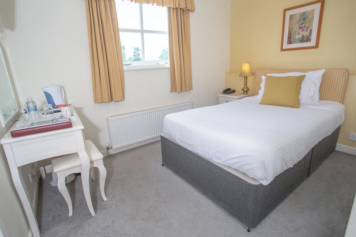 A neatly arranged bedroom with a bed, bedside table, lamp, and a desk with a chair.