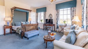 A well-appointed bedroom with a four-poster bed, a sitting area with a sofa and armchairs, a small dining table with a fruit bowl, and a television. - Diglis House Hotel (Worcester)