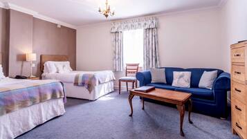 Habitación de hotel con dos camas, un sofá azul, un aparador de madera, una mesa de centro de madera, una silla y una ventana con cortinas.