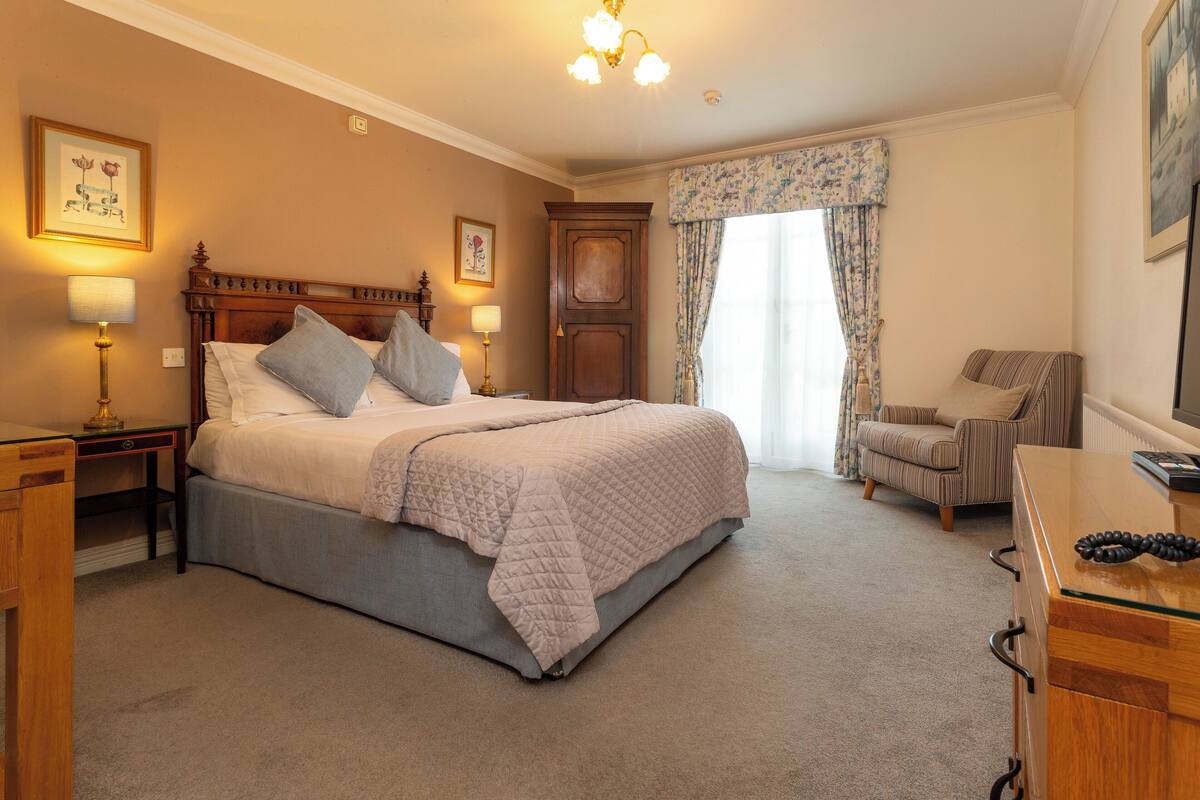 A bedroom with a large bed, a nightstand, a dresser, a chair, and a window with curtains.