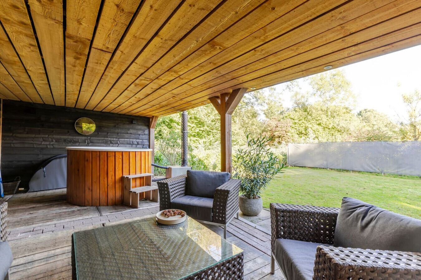 Un patio al aire libre con suelo de madera, un jacuzzi, mobiliario de mimbre y una maceta de piedra.