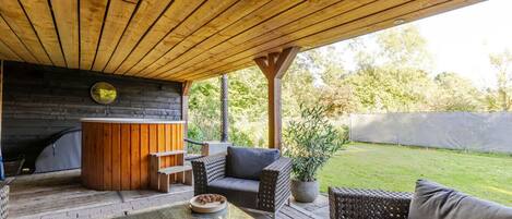 Un patio al aire libre con suelo de madera, un jacuzzi, mobiliario de mimbre y una maceta de piedra.