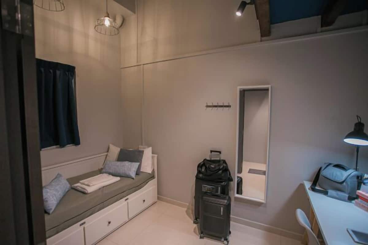 A compact hotel room with a bed, a desk, a chair, a suitcase, and a mirror.